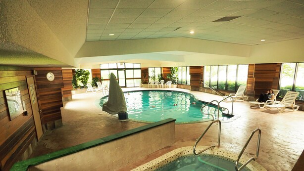 An indoor swimming pool with a tiled edge, lounge chairs, and a clock on the wall. - Evergreen Resort (Cadillac)
