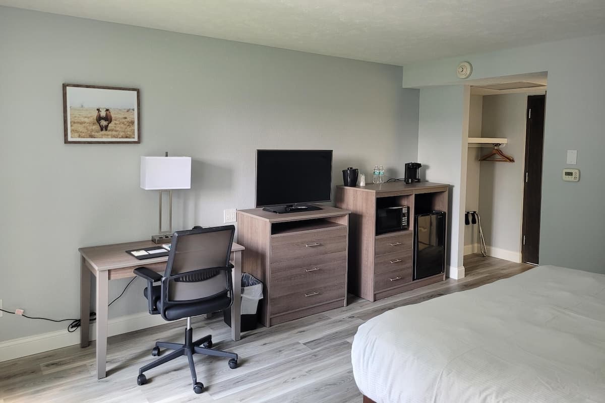 Ein Hotelzimmer mit Bett, Schreibtisch mit Computer, Stuhl, Fernseher, Lampe, Mikrowelle und einem kleinen Schrank.