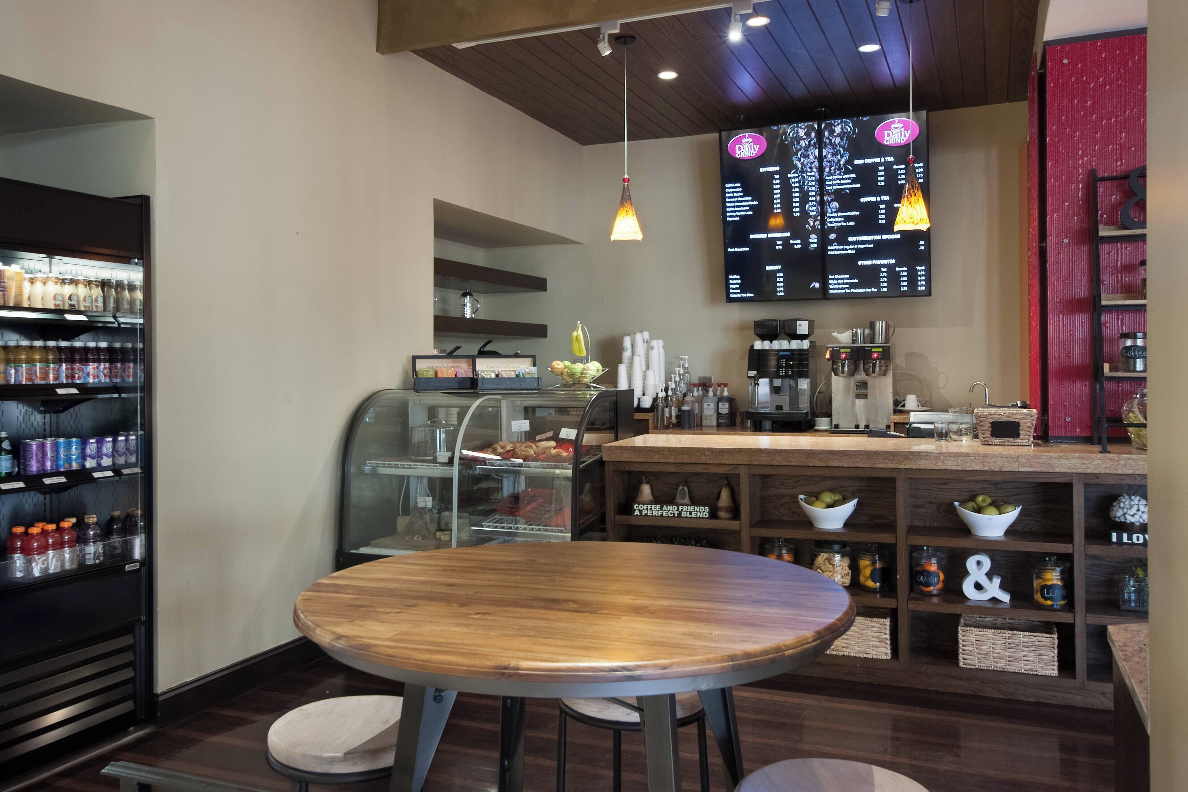 Un café avec une table et des chaises en bois, un tableau affichant le menu, des étagères remplies de boissons et de pots, et une machine à café.