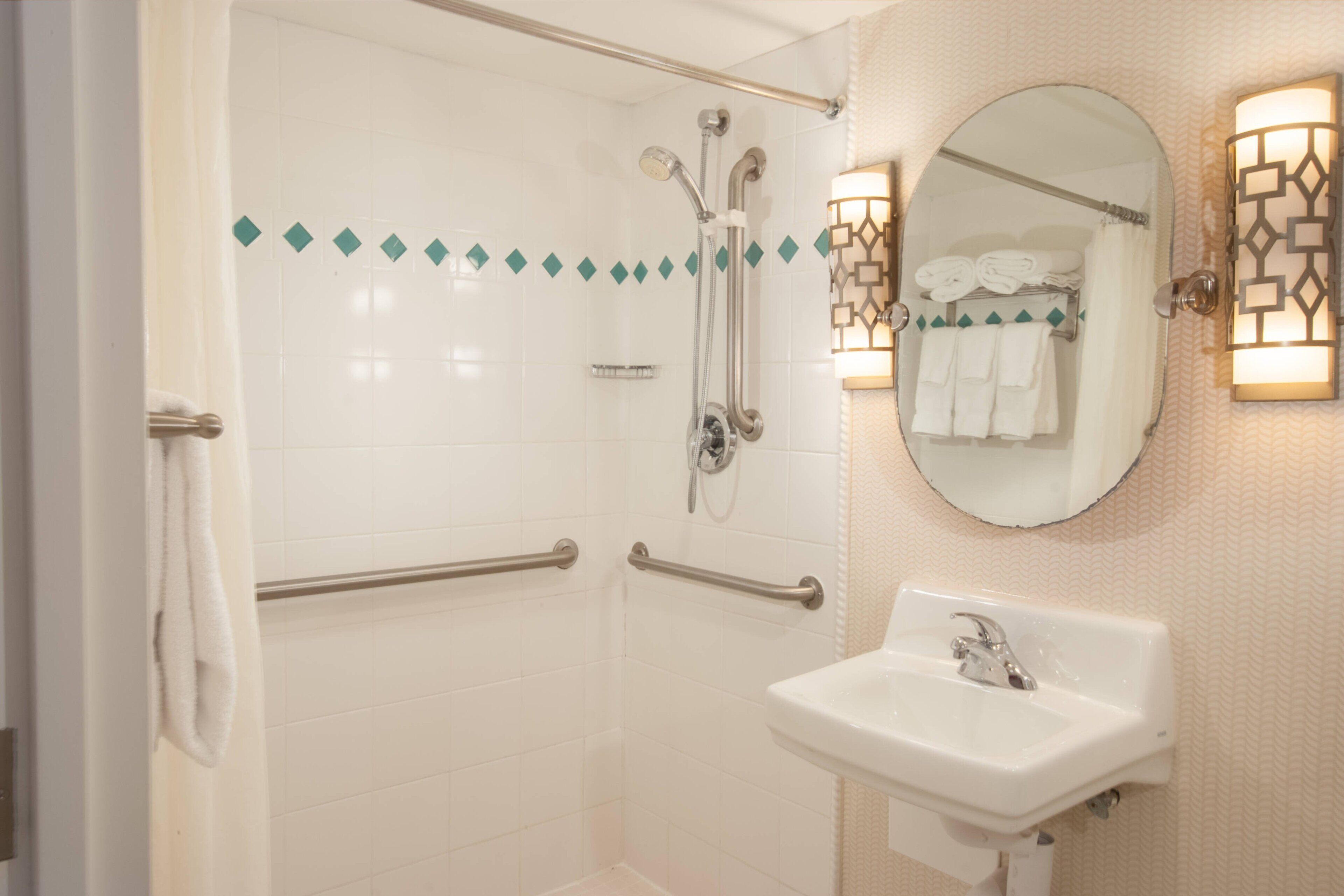 A bathroom with a walk-in shower, grab bars, a sink, and a mirror with a towel rack.