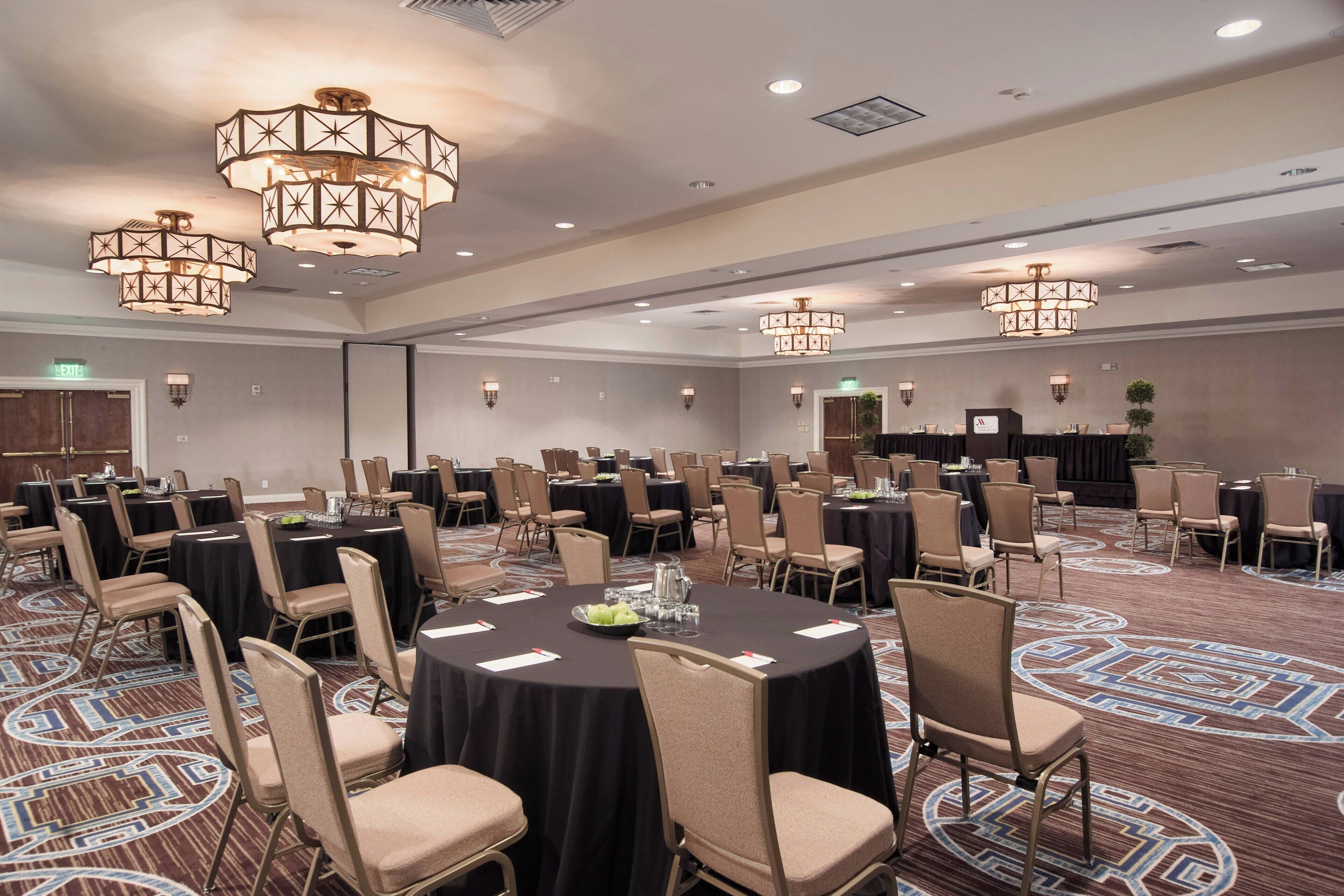 A large conference room with round tables, chairs, and chandeliers.