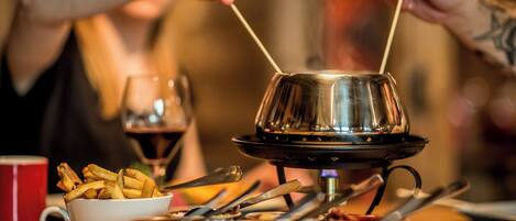 A dining table with a metal fondue pot, a bowl of fries, and a glass of red wine.