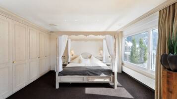 A bedroom with a four-poster bed, a large window with a view of trees, and a wooden nightstand with a lamp.
