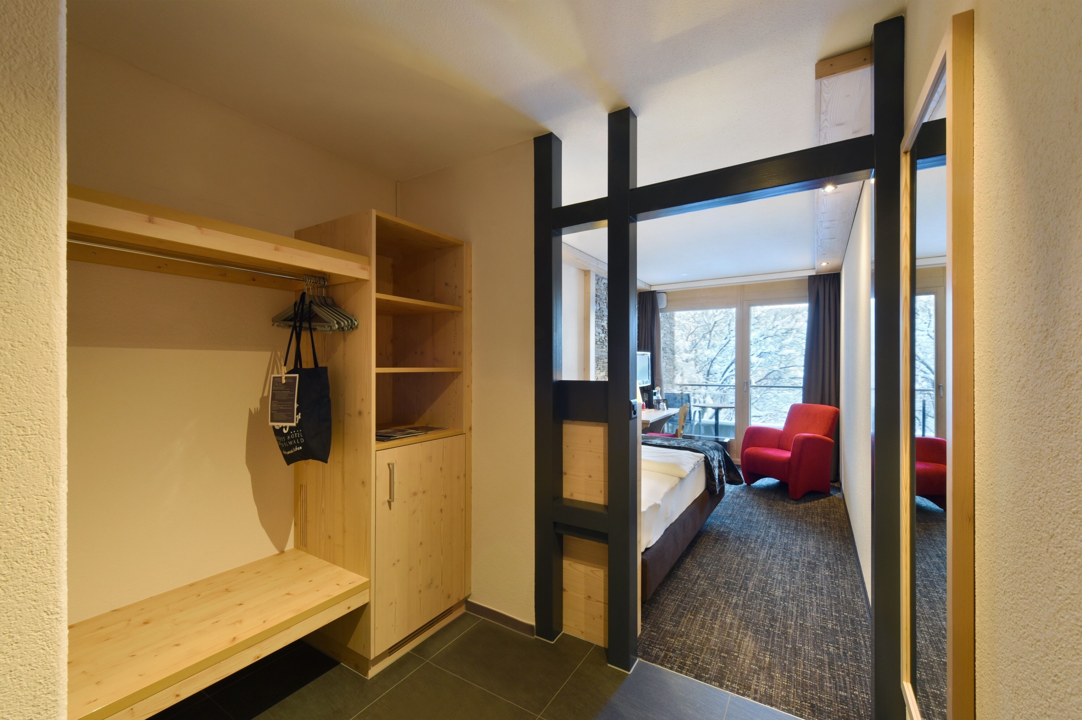 Een hotelkamer met een houten garderobe, een klein bureau, een bed en een rode stoel.
