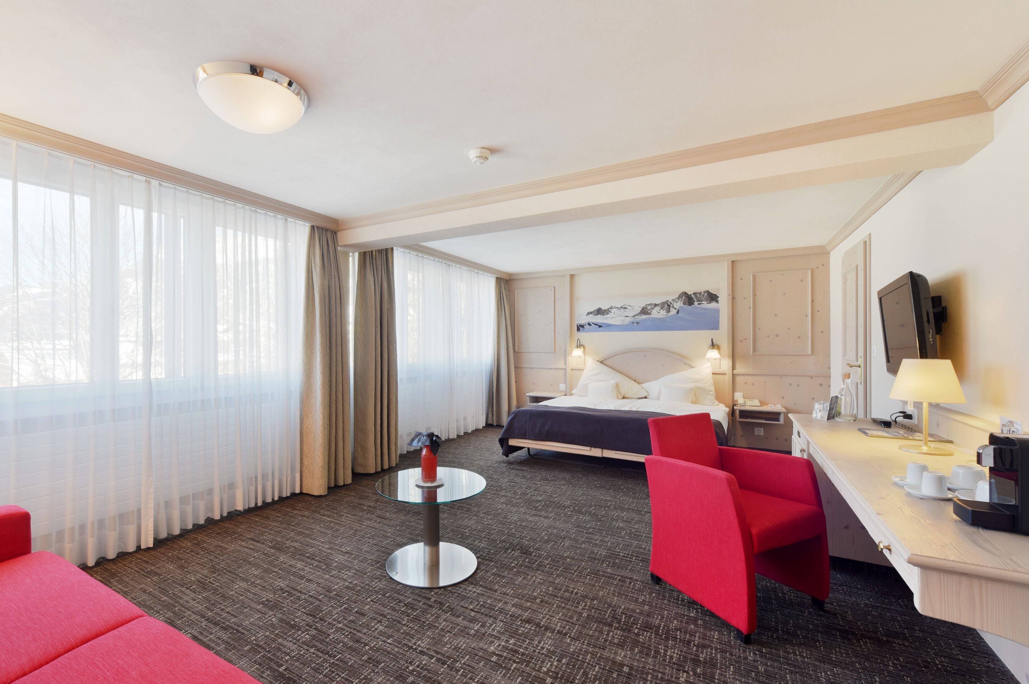 Ein Hotelzimmer mit einem Bett, einem Schreibtisch, einem Sessel, einem kleinen Tisch und einem Fenster mit Vorhängen.