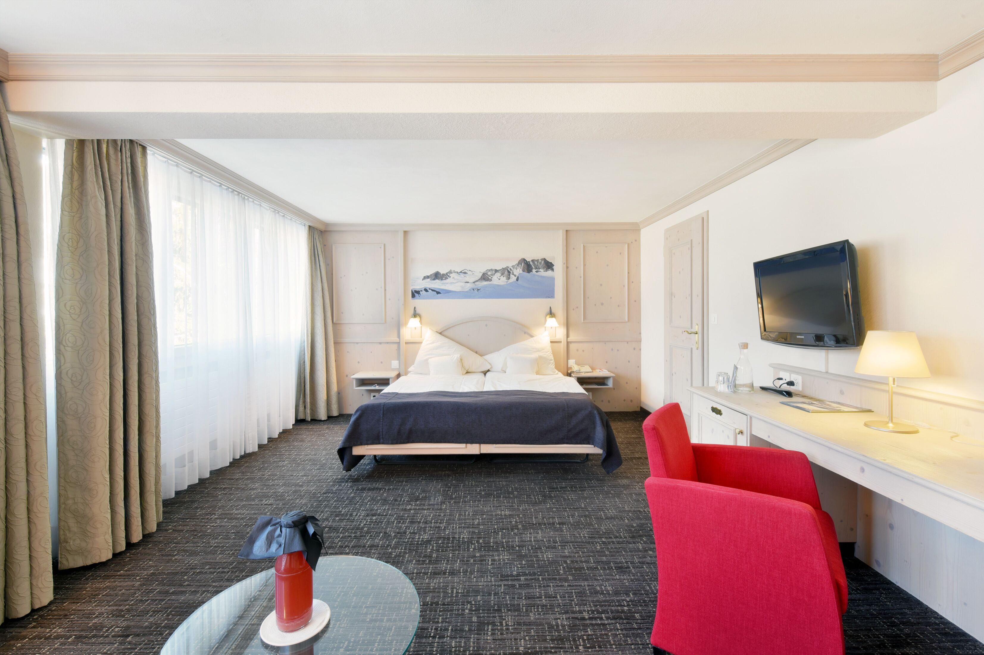 A hotel room with a bed, a desk, a TV, and a chair.