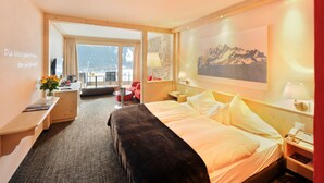 A hotel room with a bed, a desk, a chair, a lamp, and a painting on the wall.