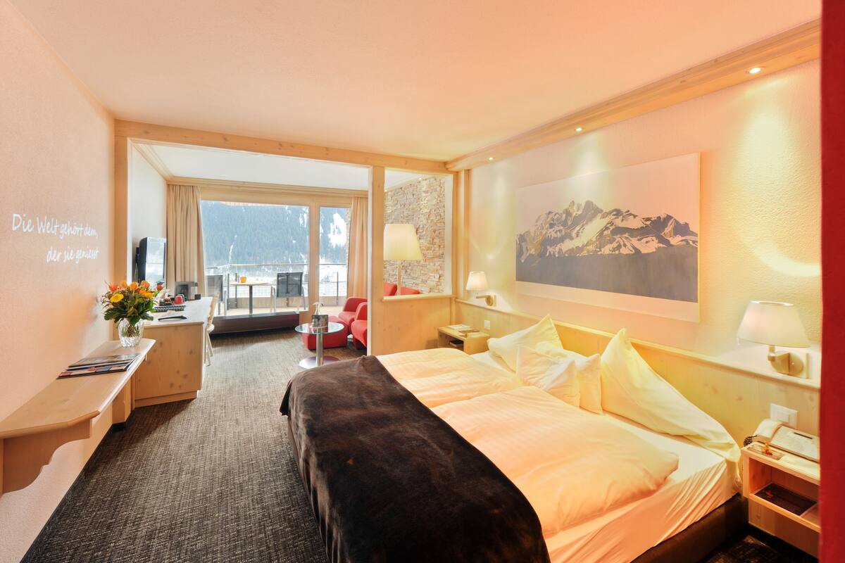 A hotel room with a bed, a desk, a chair, a lamp, and a painting on the wall.