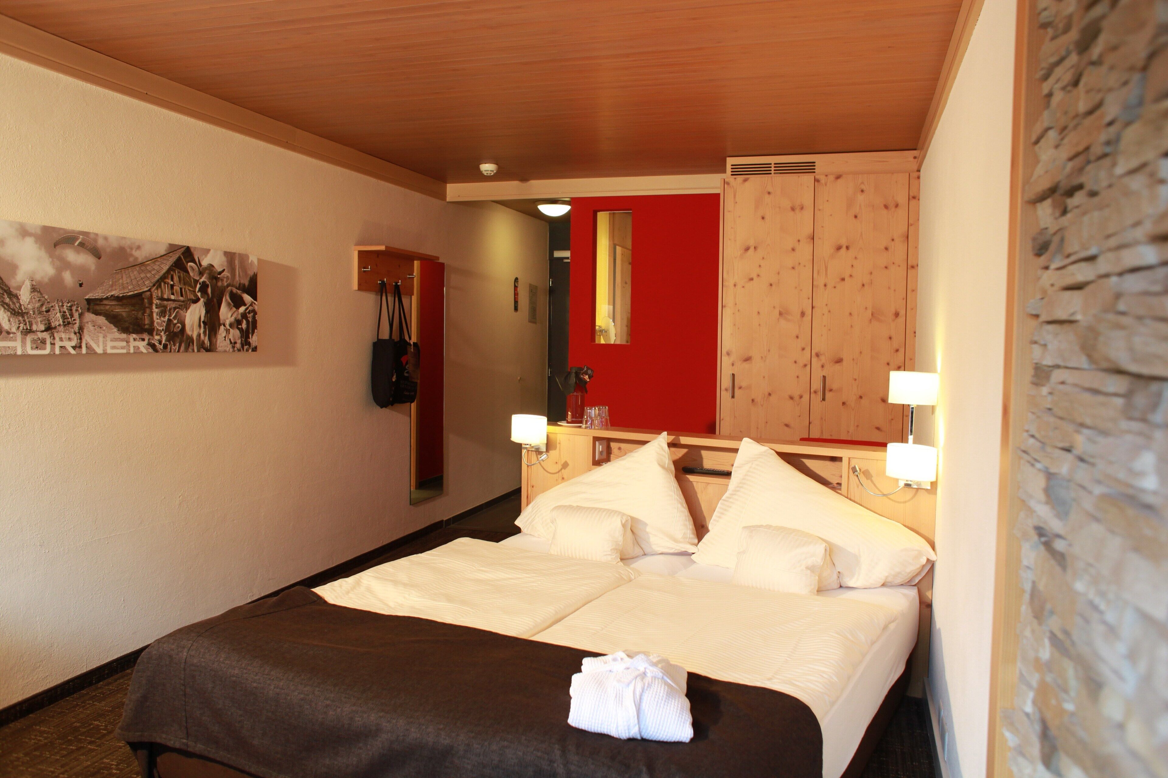 Ett hotellrum med en säng, en träpanel som huvudgavel, en röd accentvägg och en tavla på väggen.