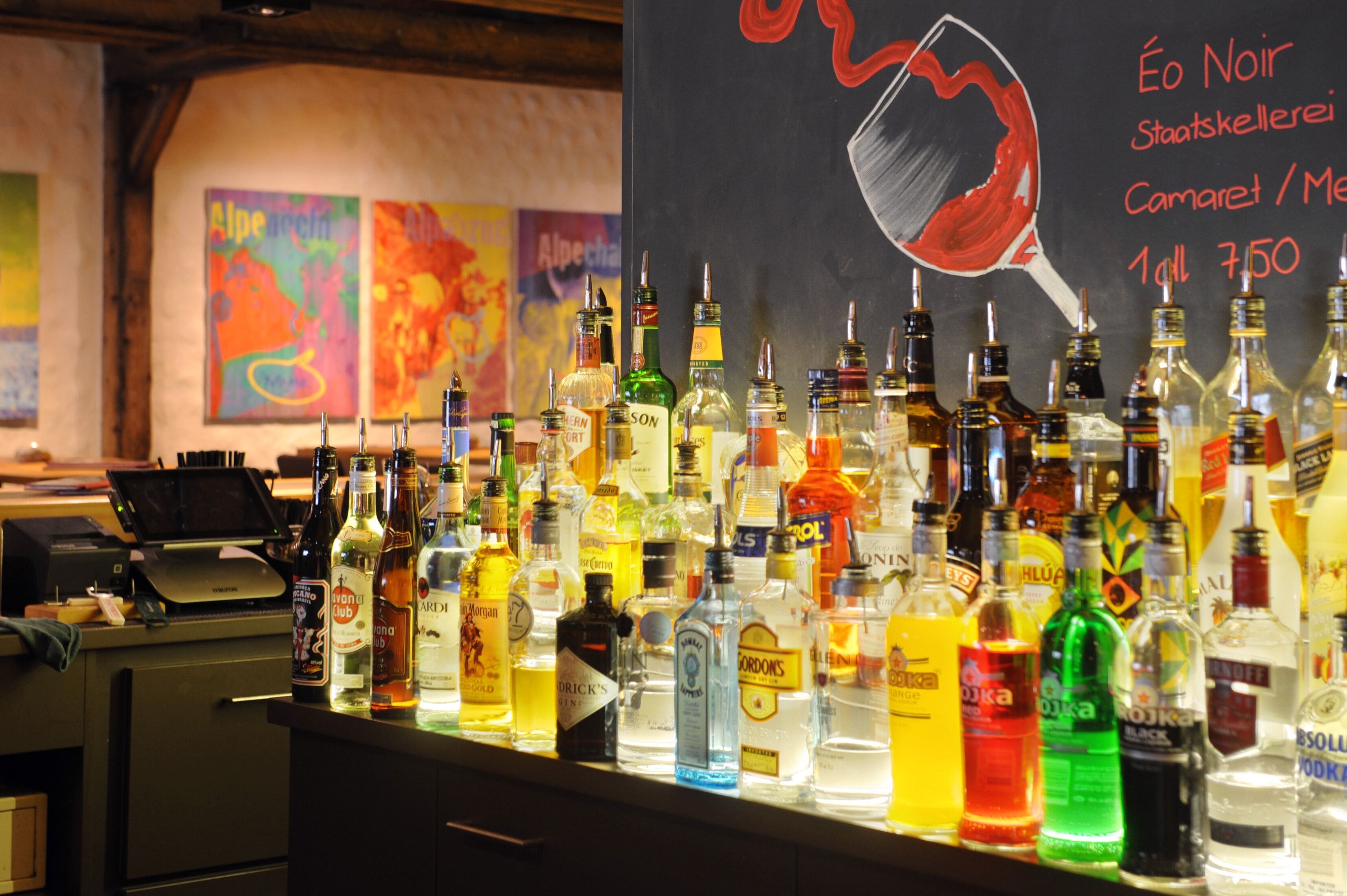 A bar counter with various liquor bottles and a chalkboard menu.