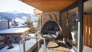 A modern outdoor seating area with a cushioned chair and a glass balustrade overlooking a snowy mountain landscape.