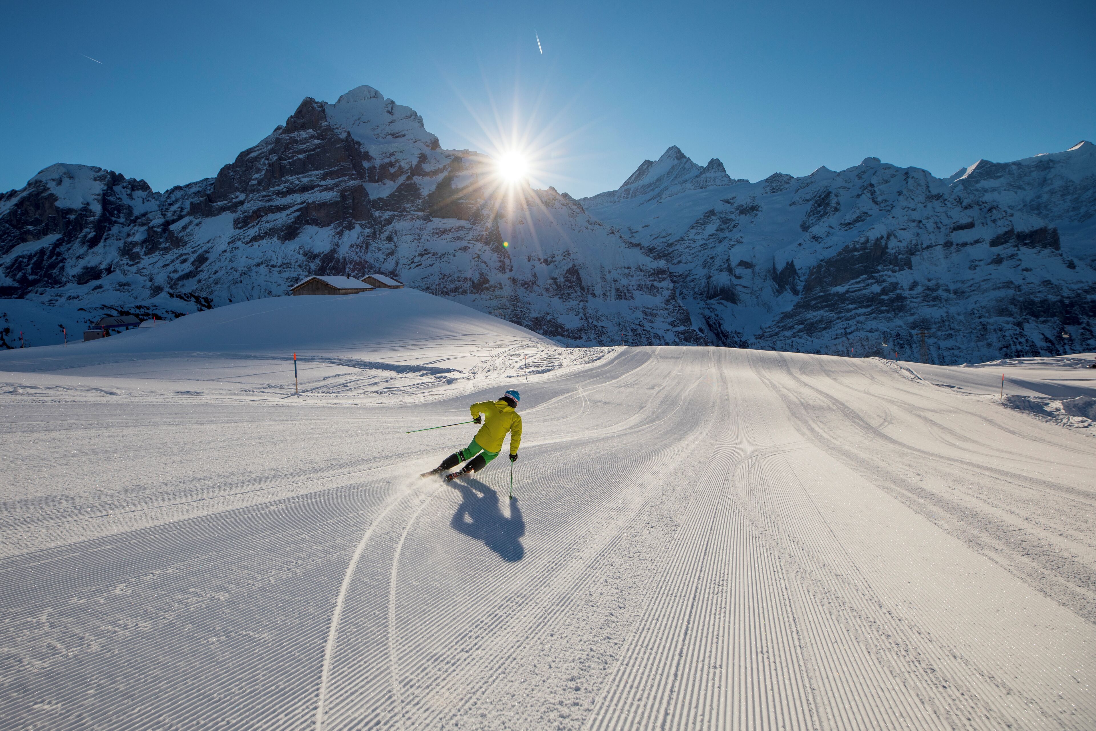 A snowy ski slope with a skier in motion, surrounded by snow-covered mountains and a clear sky.