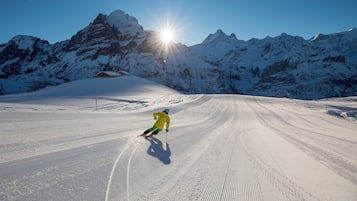 A snowy ski slope with a skier in motion, surrounded by snow-covered mountains and a clear sky.