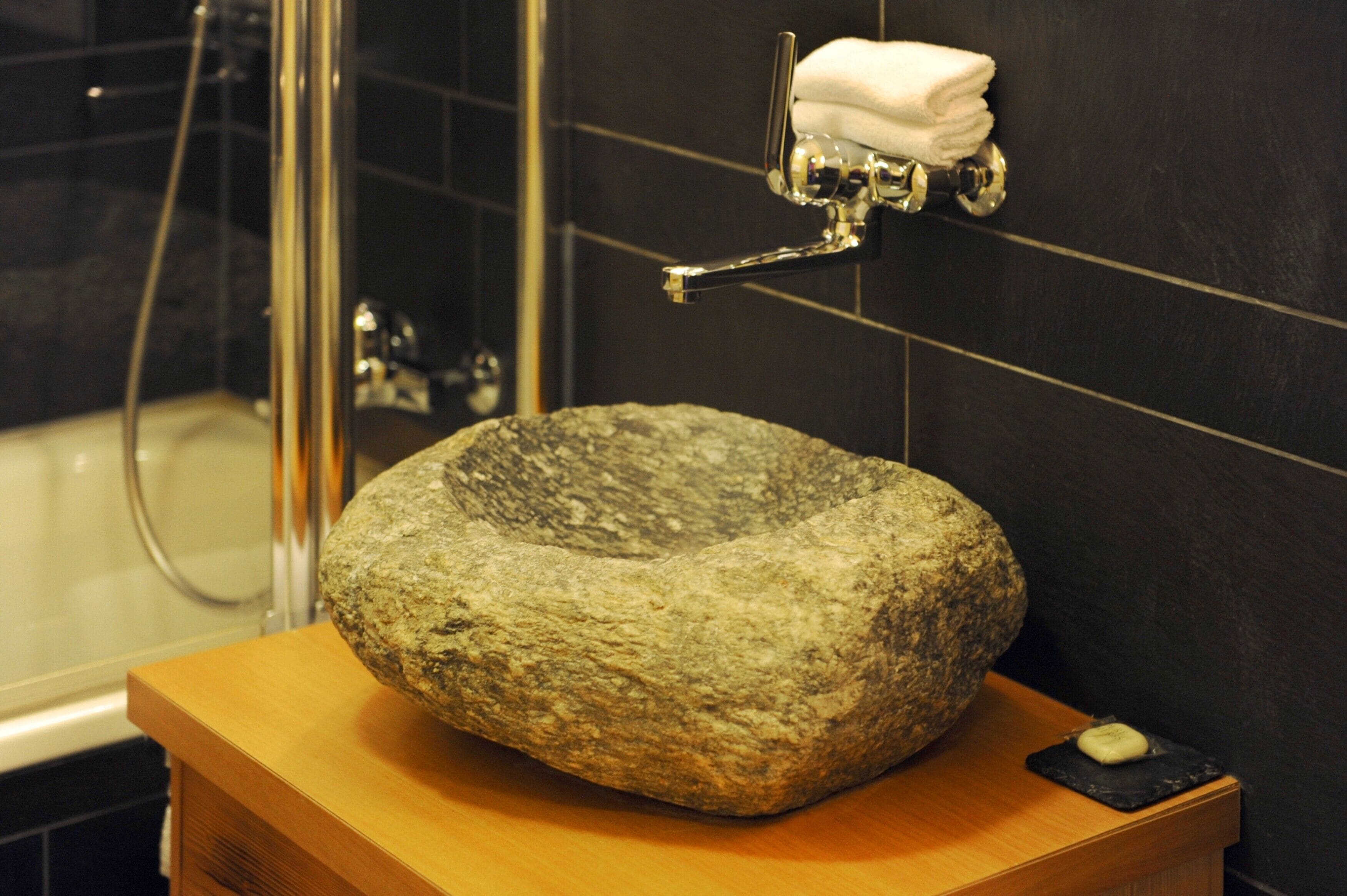 A bathroom with a stone basin, a towel rack with folded towels, and a soap dish.