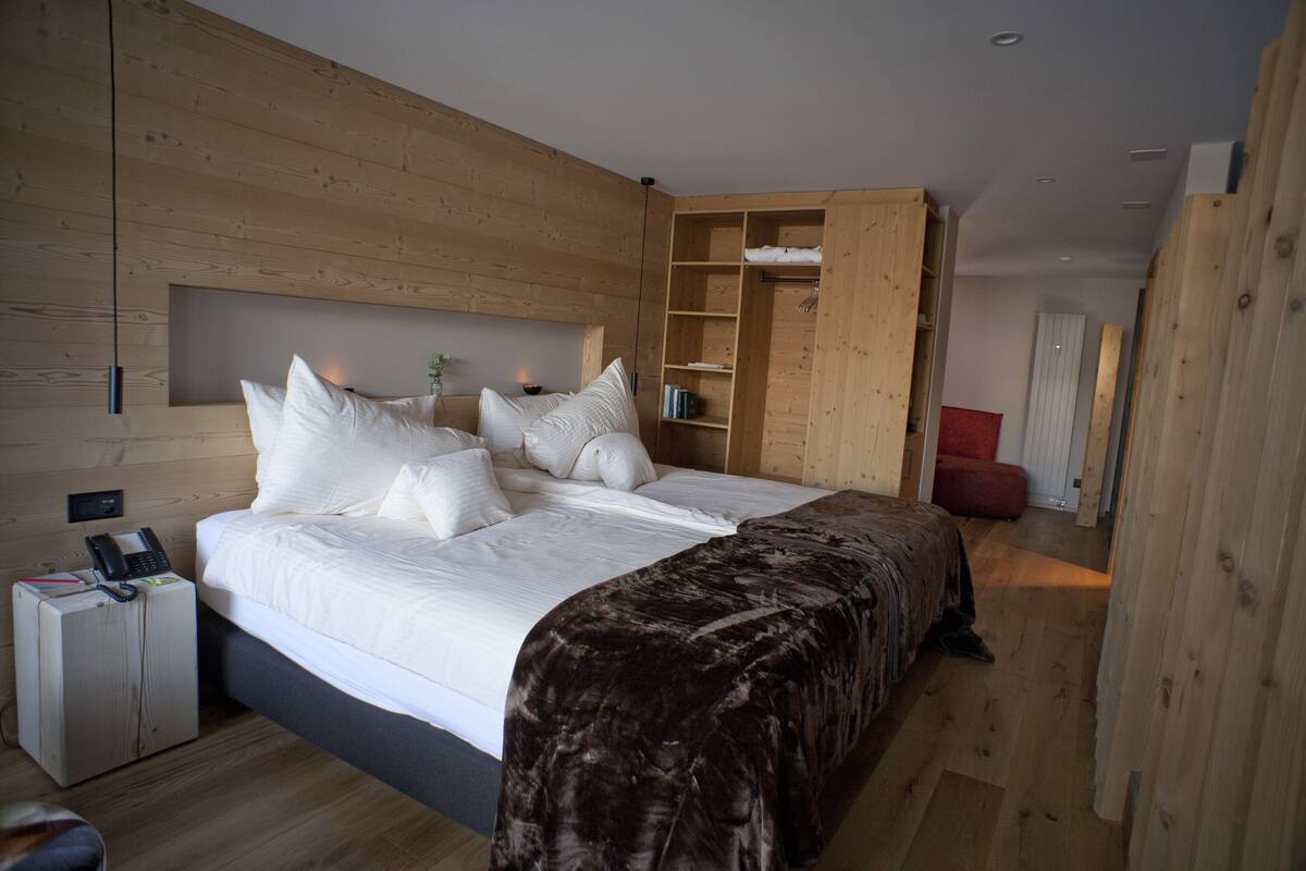 A modern bedroom with a large bed, wooden headboard, built-in shelving, and a small bedside table with a phone.
