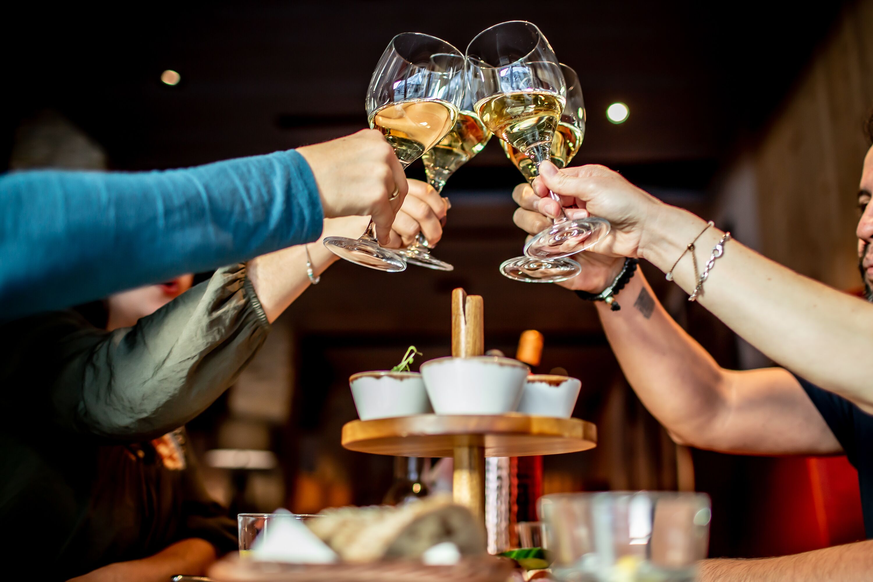 A group of people toasting with wine glasses at a table with a tiered serving tray.