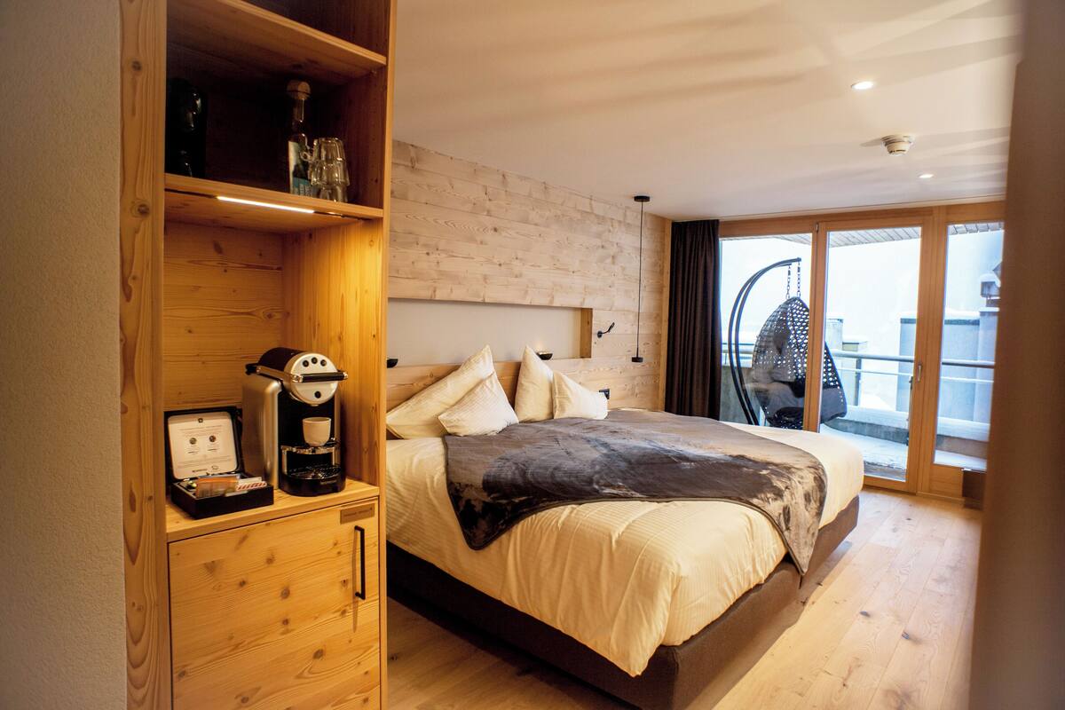 A modern bedroom with a wooden bed, a coffee machine, and a view of the outside balcony.