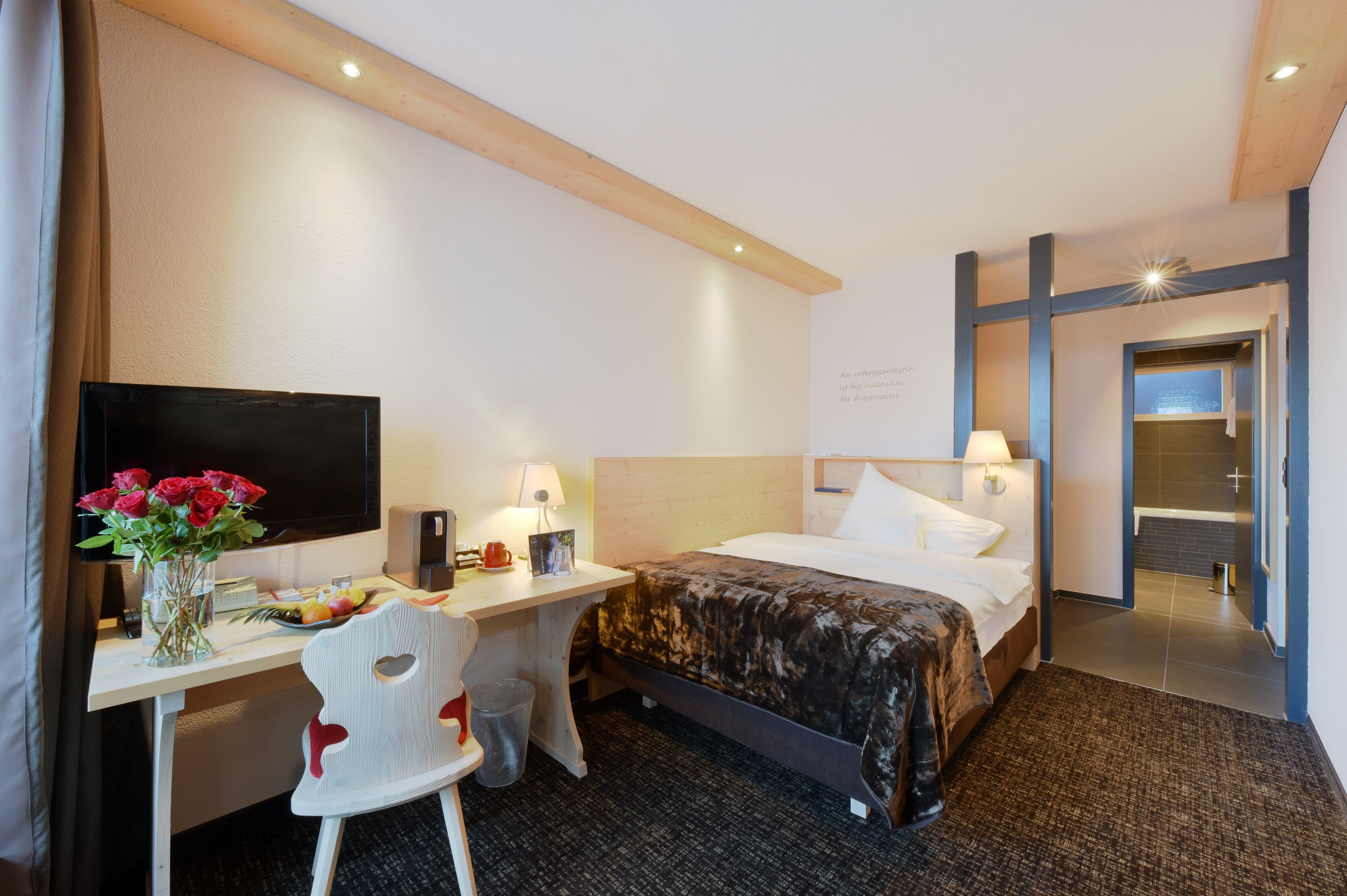 A hotel room with a bed, desk, chair, TV, and a bathroom visible through an open door.