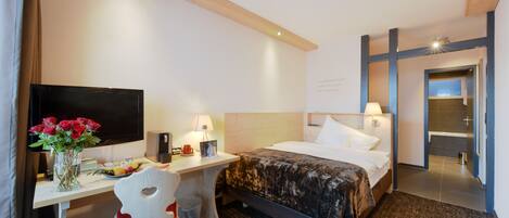 A hotel room with a bed, desk, chair, TV, and a bathroom visible through an open door.