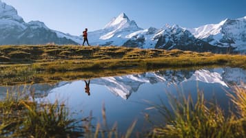 A person hiking in a mountainous area with snow-capped peaks in the background and a reflective water body in the foreground.