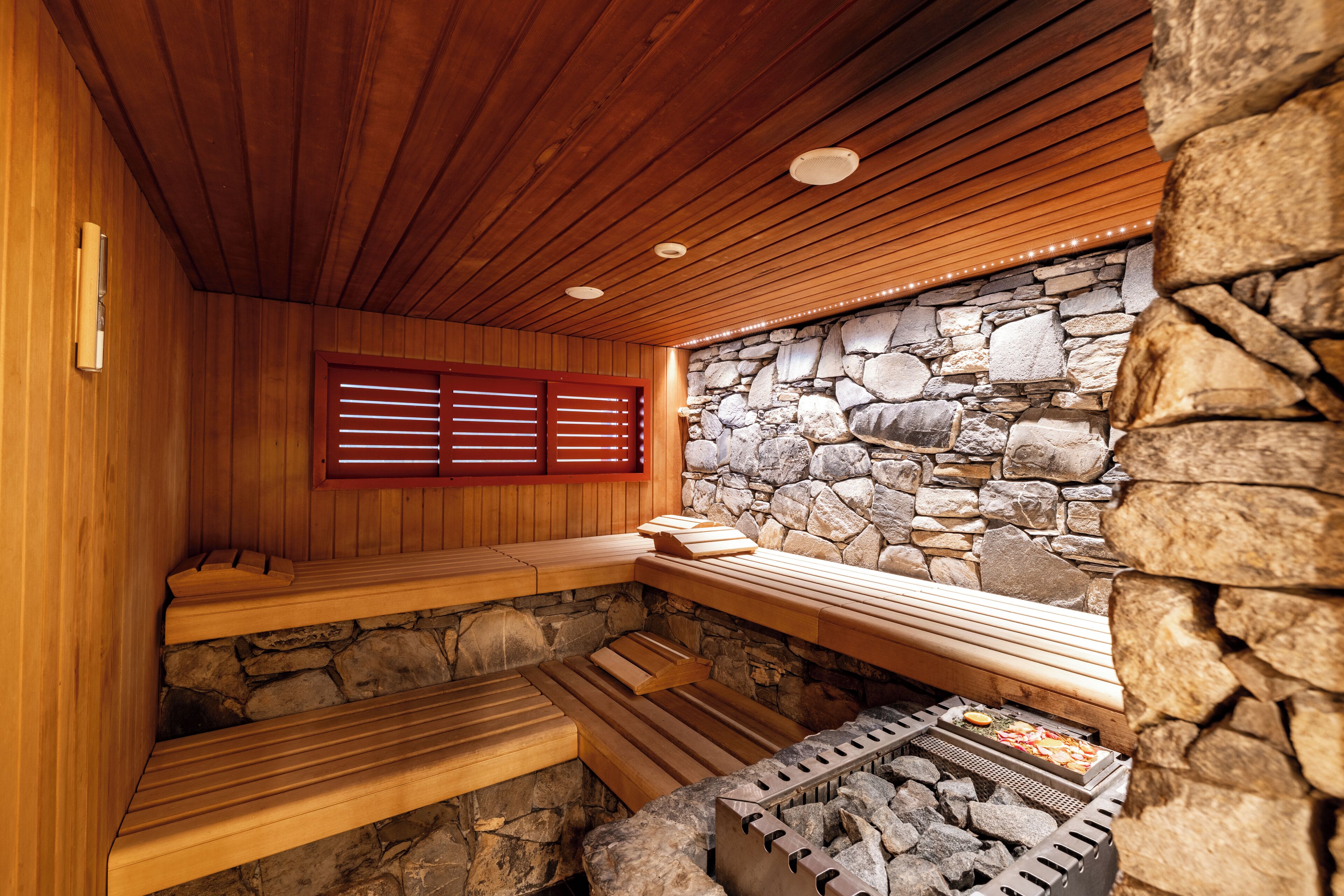 A sauna with wooden benches, a stone wall, and a grill area.