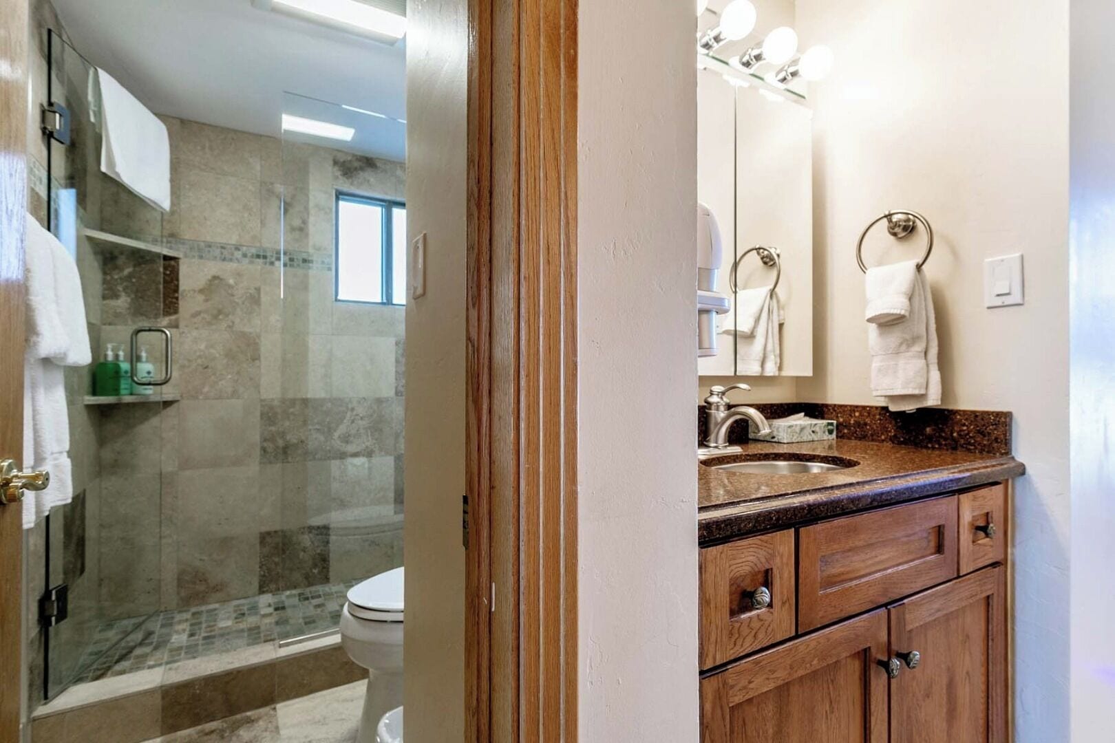 Un baño con cabina de ducha de vidrio, lavamanos con encimera de granito y armarios de madera.
