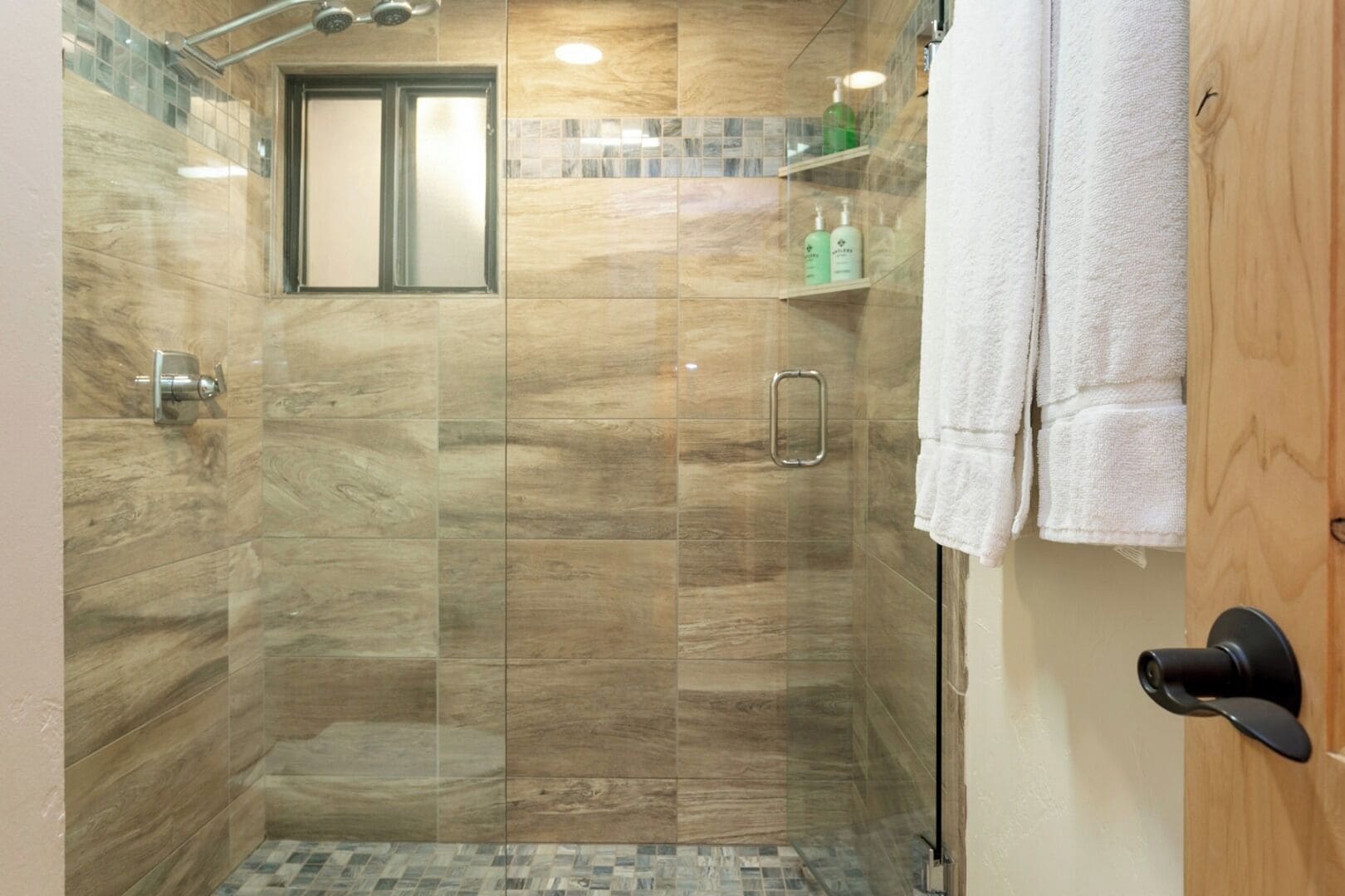 Une douche à l’italienne avec une porte en verre, une petite fenêtre et une étagère pour les articles de toilette.