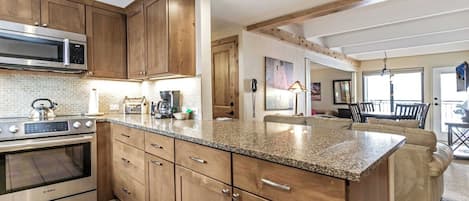 Una cocina moderna con armarios de madera, encimera de granito y electrodomésticos de acero inoxidable, incluyendo un horno y microondas Bosch.
