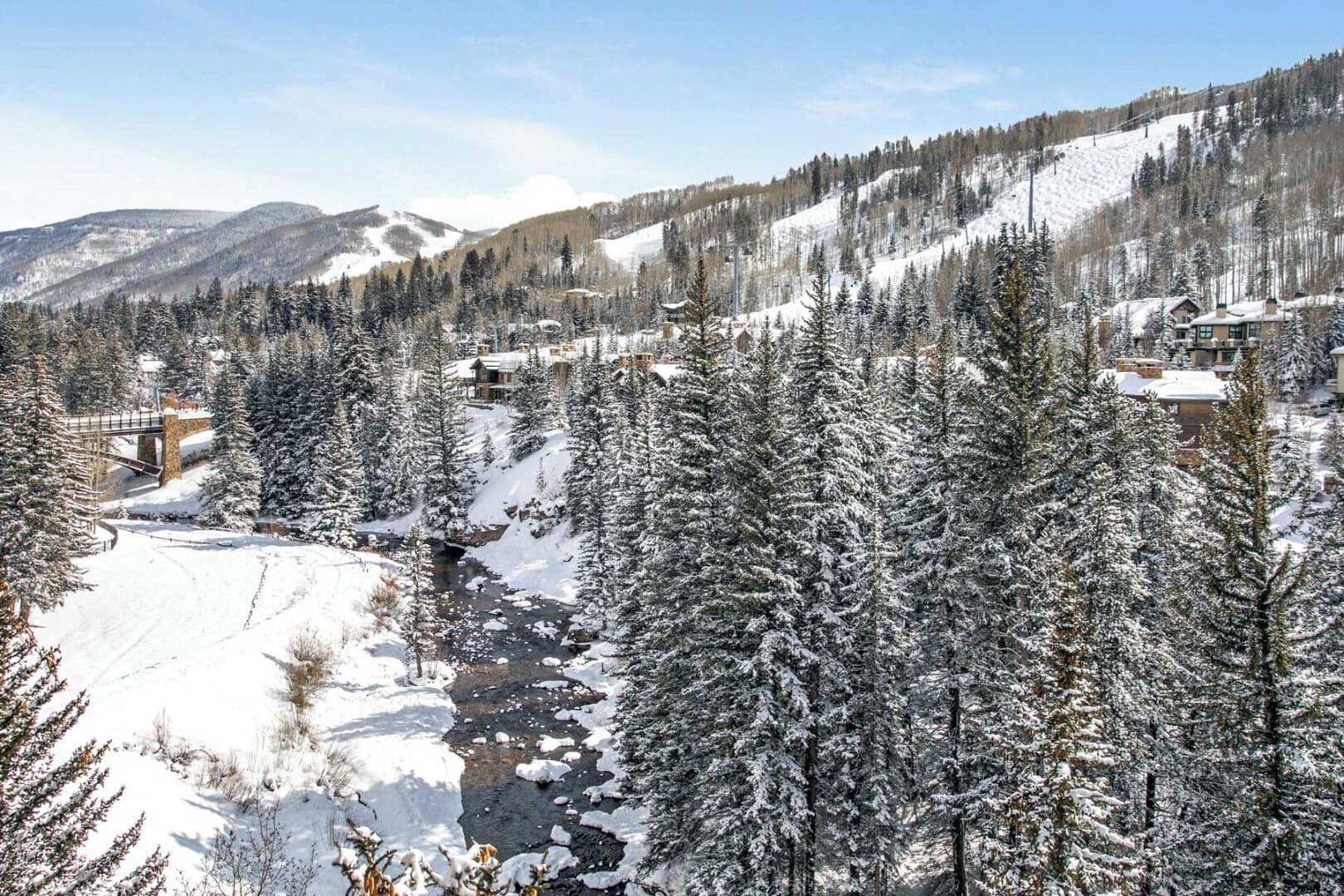 A snow-covered mountain landscape with a river, trees, and buildings in the background.