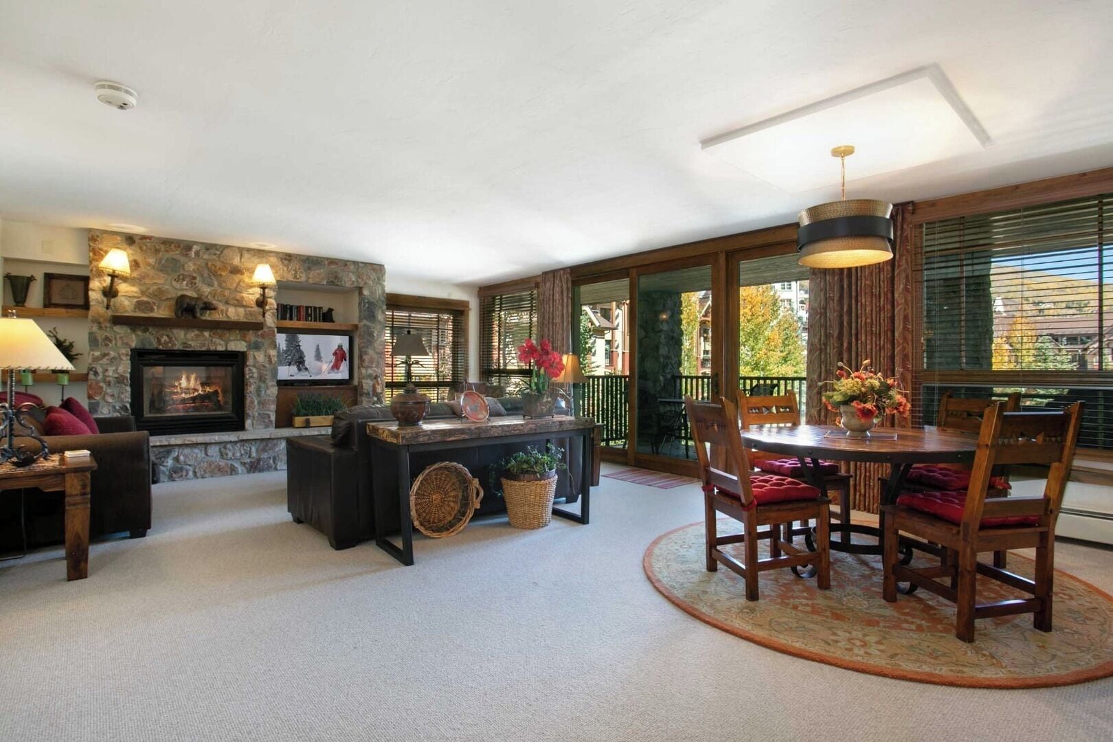 A cozy living room with a fireplace, a dining area with a round table and chairs, and a stone wall.