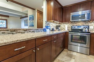 A modern kitchen with wooden cabinets, granite countertops, a stainless steel oven, and a microwave.