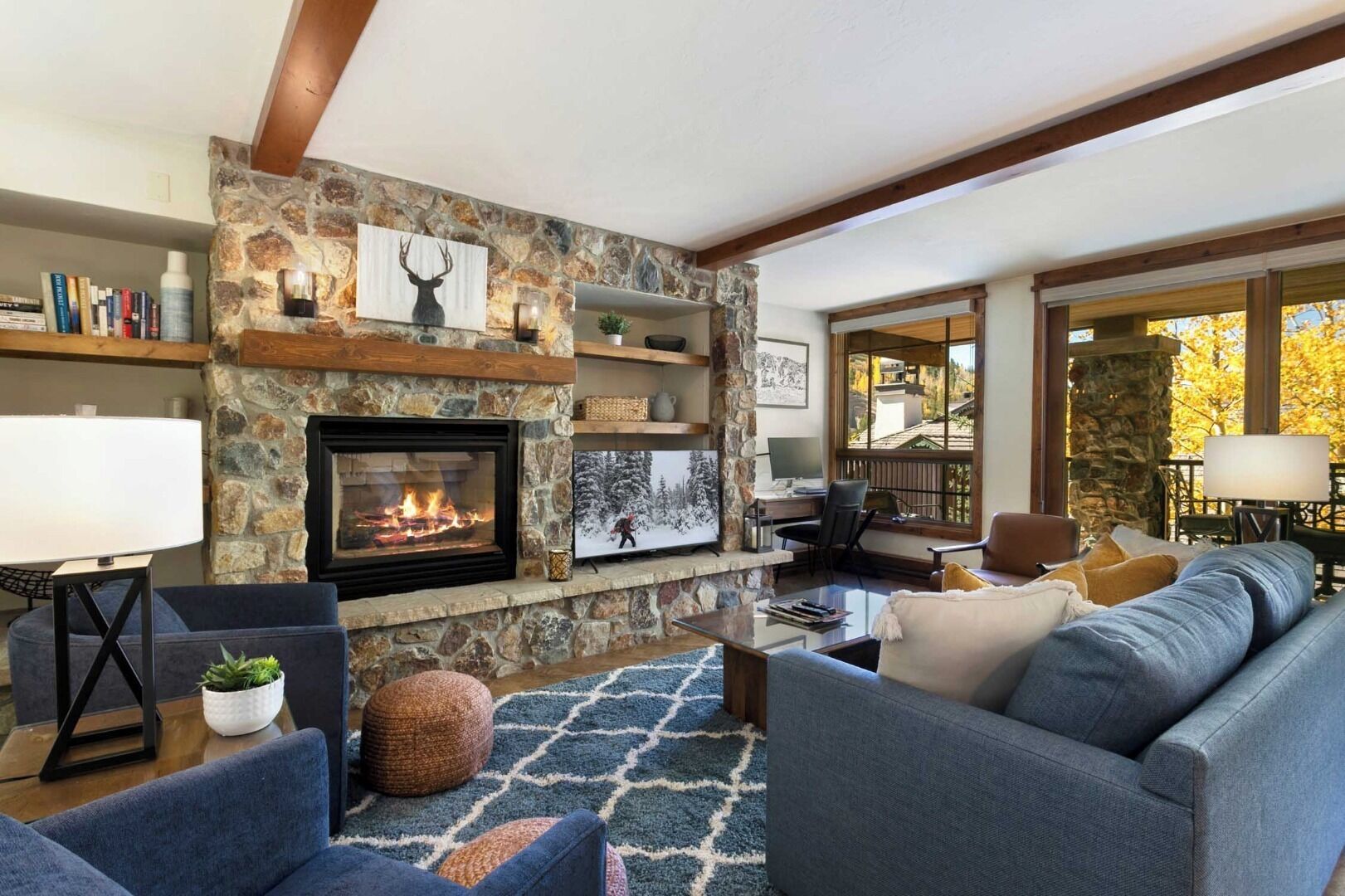 A cozy living room with a stone fireplace, comfortable seating, and a view of the outdoors.