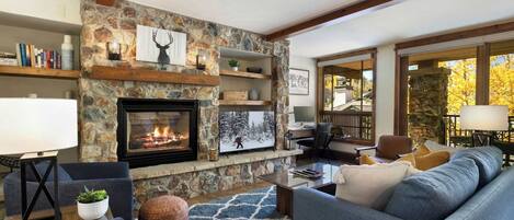 A cozy living room with a stone fireplace, comfortable seating, and a view of the outdoors.