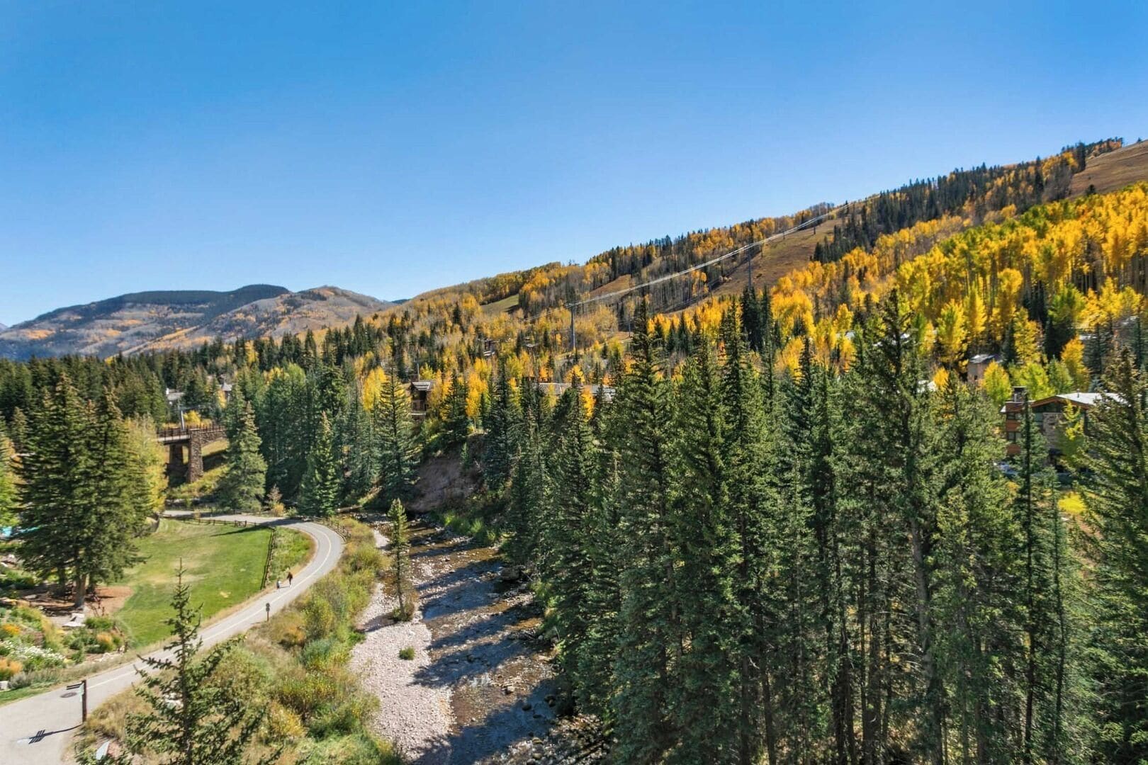 A mountainous landscape with a winding road, dense forest, and a small building with a stone structure.