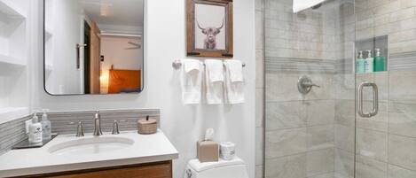 A modern bathroom with a large mirror, a sink with toiletries, a toilet, and a glass-enclosed shower.