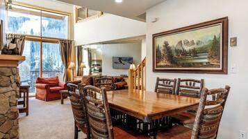 A dining area with a large wooden table and rustic chairs, a fireplace, and a scenic view through large windows.