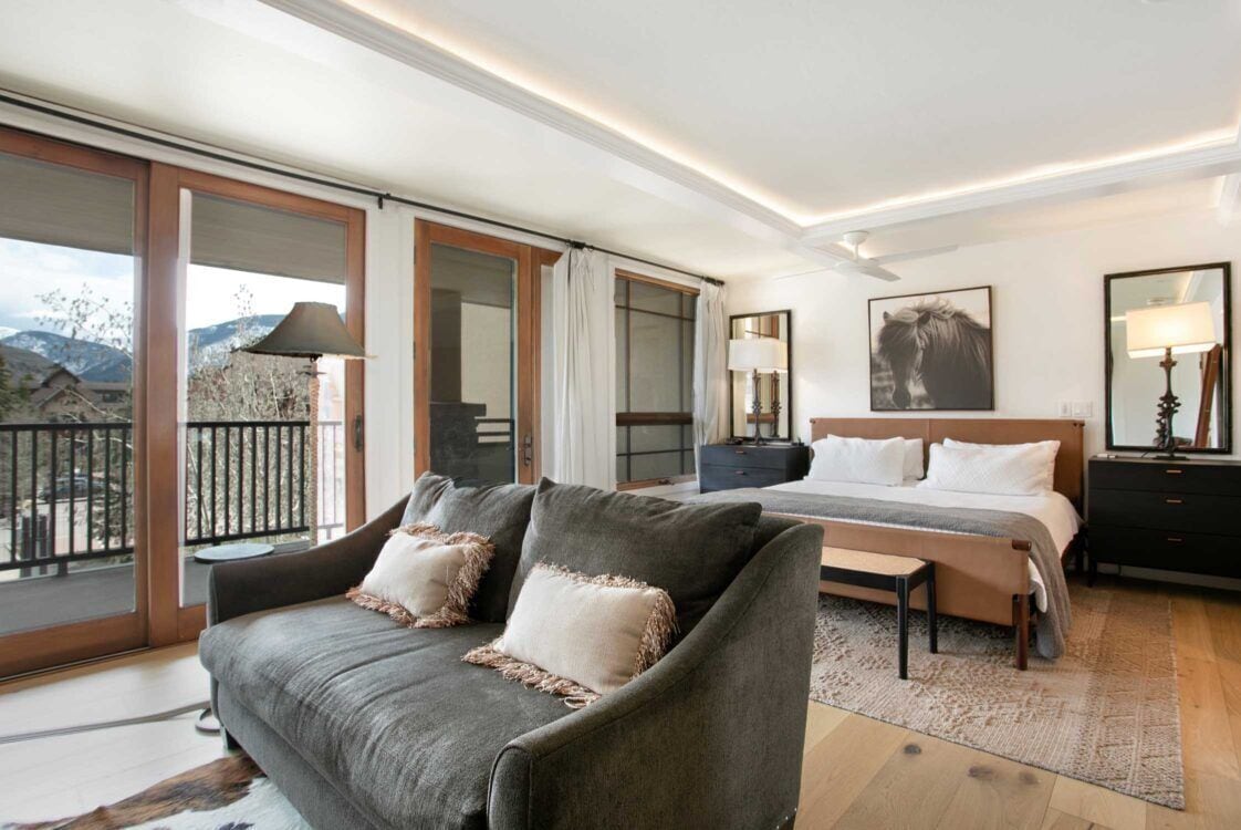 A modern hotel room with a large bed, a sofa, and a balcony with a view of the mountains.