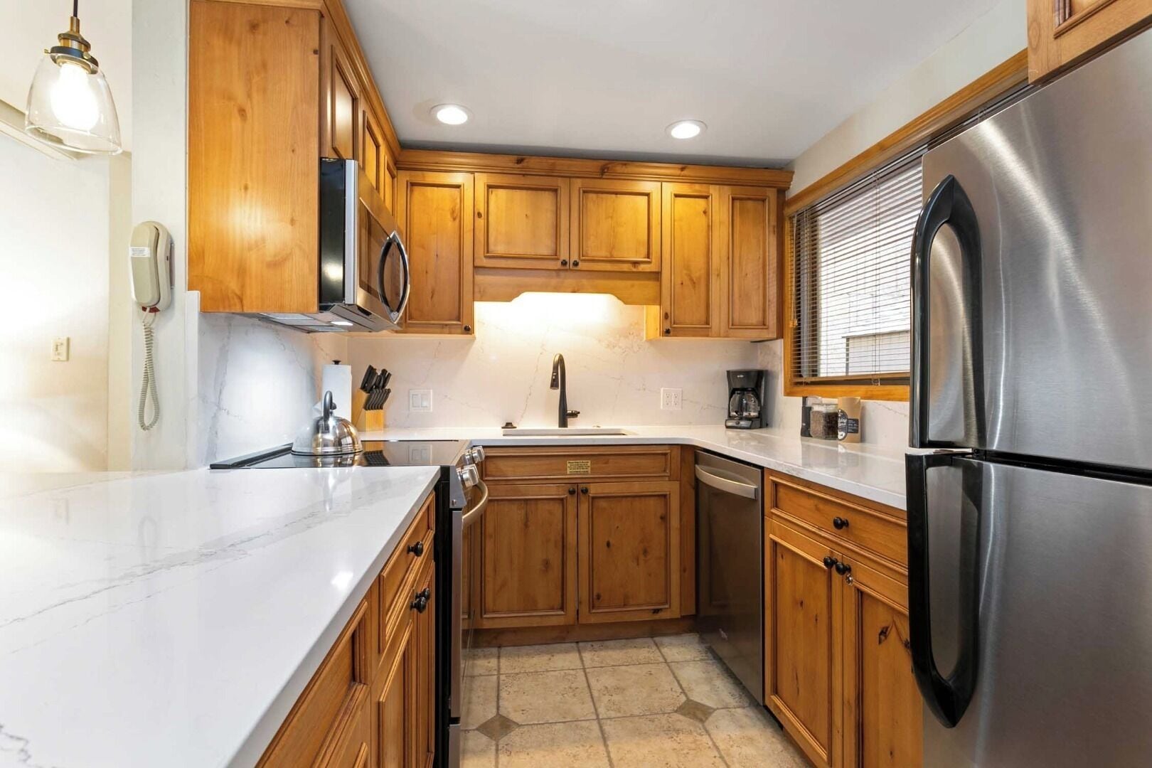 A kitchen with wooden cabinets, a stainless steel refrigerator, a marble countertop, and a built-in dishwasher.