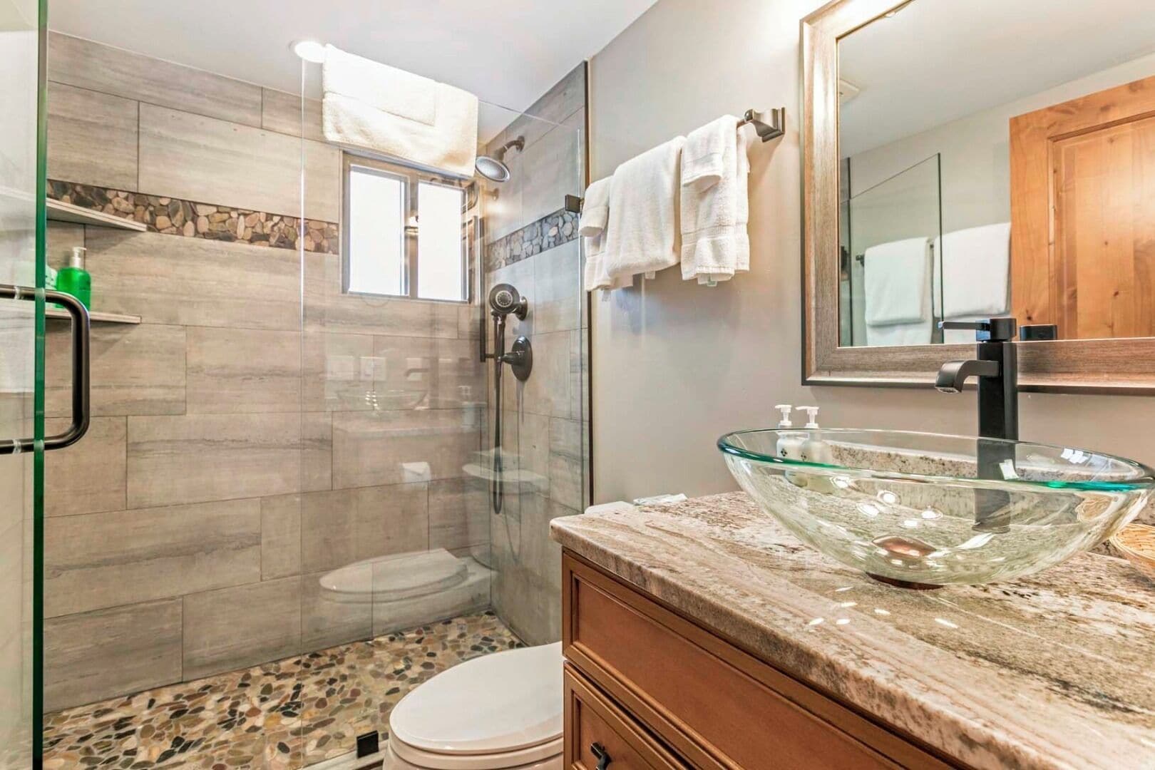 Un baño moderno con un lavabo de vidrio, ducha a ras de suelo y un inodoro.