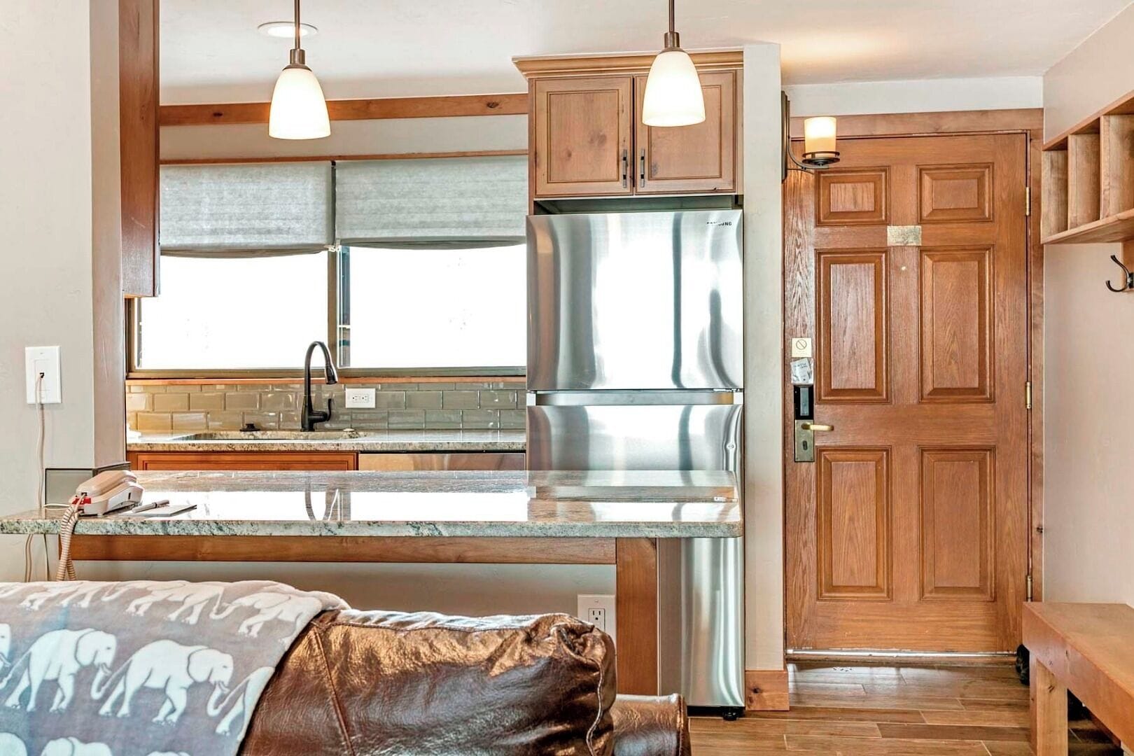 A modern kitchen with wooden cabinets, a stainless steel refrigerator, and pendant lights.