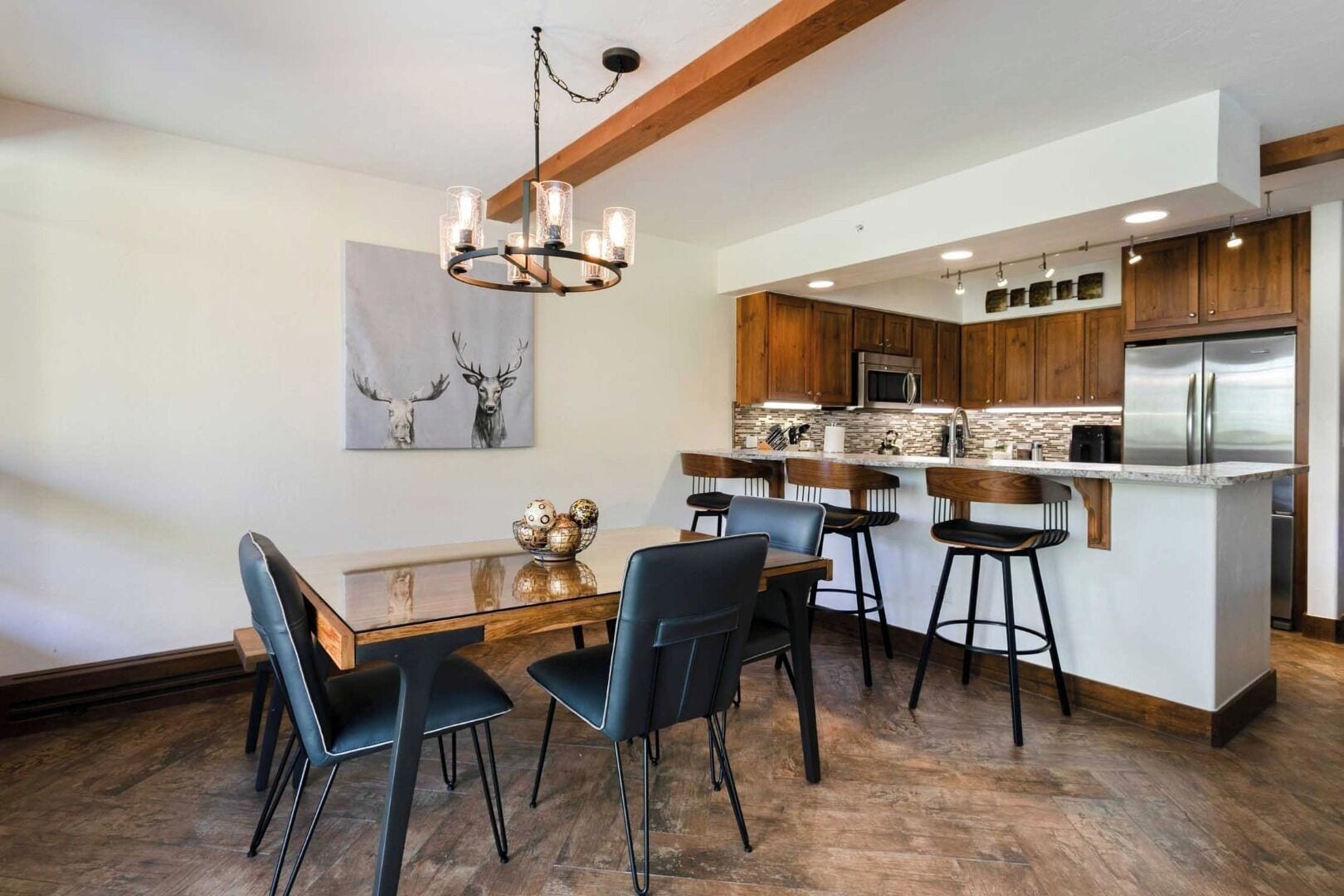 A modern kitchen with wooden cabinets, a stainless steel refrigerator, and a dining area with a glass table and black chairs.