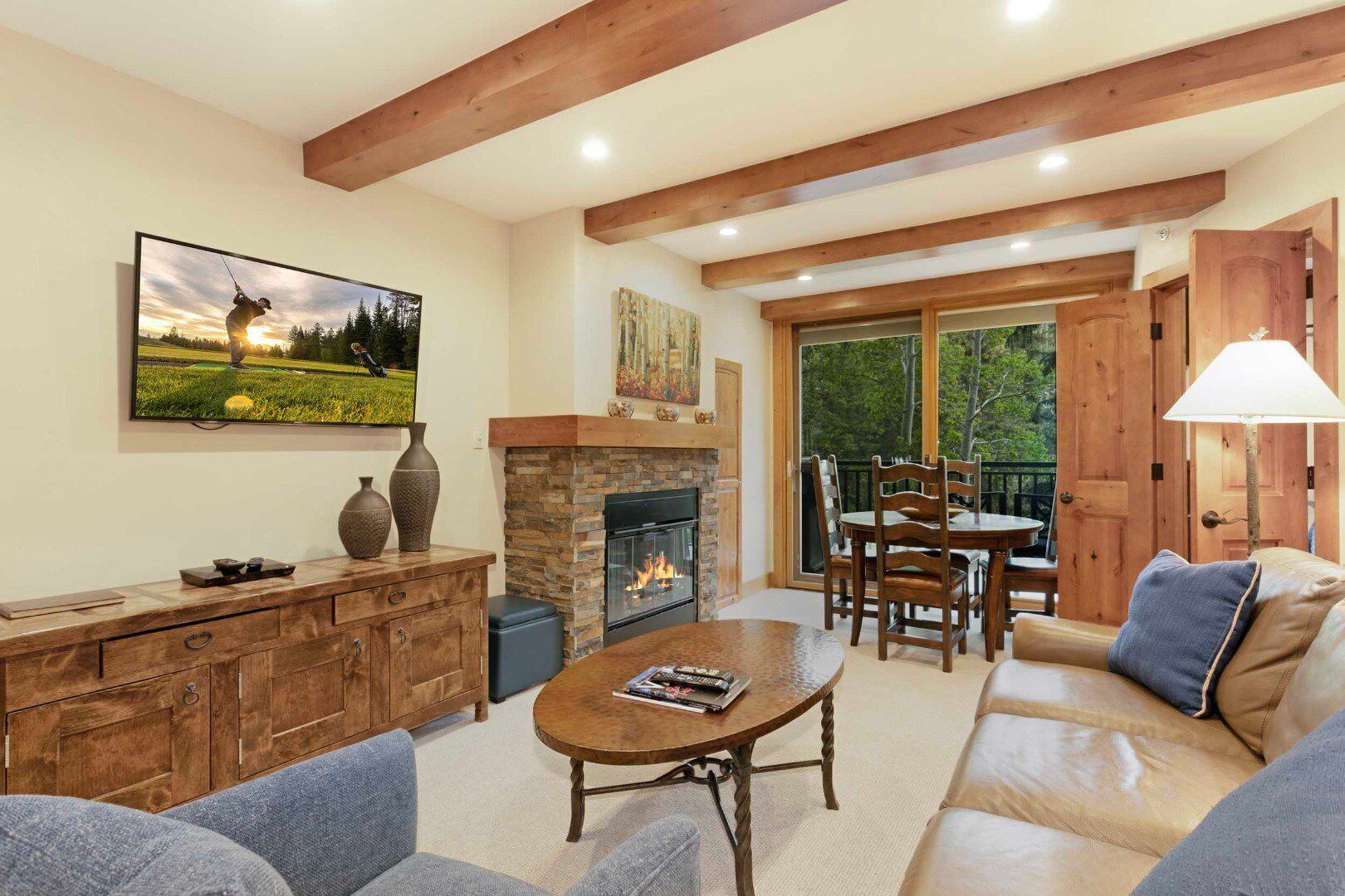 A cozy living room with a fireplace, wooden furniture, and a large window offering a view of the outdoors.