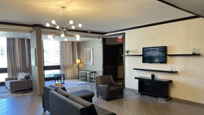 A modern hotel lobby with a sofa, chairs, a TV, and a chandelier.