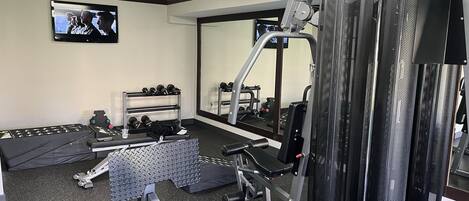 Un gimnasio con diferentes equipos de ejercicio, un televisor y un espejo.