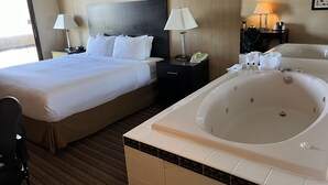 A hotel room with a large bed, a separate bathroom with a bathtub, two bedside lamps, a telephone, and a small table with toiletries.