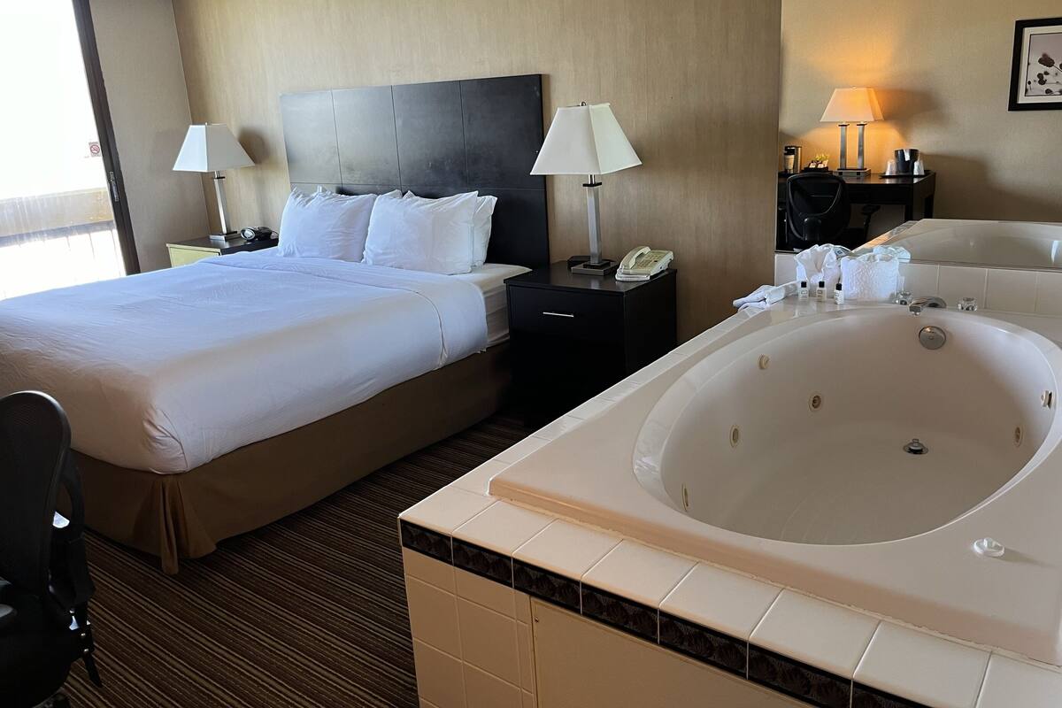 Habitación de hotel con una cama grande, baño privado con bañera, dos lámparas de noche, teléfono y una mesita de noche con artículos de aseo.
