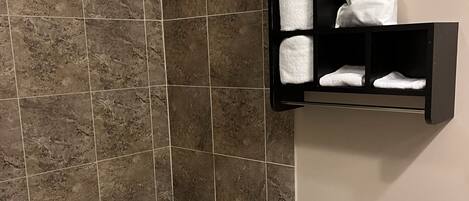 A bathroom with a bathtub, toilet, and a shelf with towels and a bag.