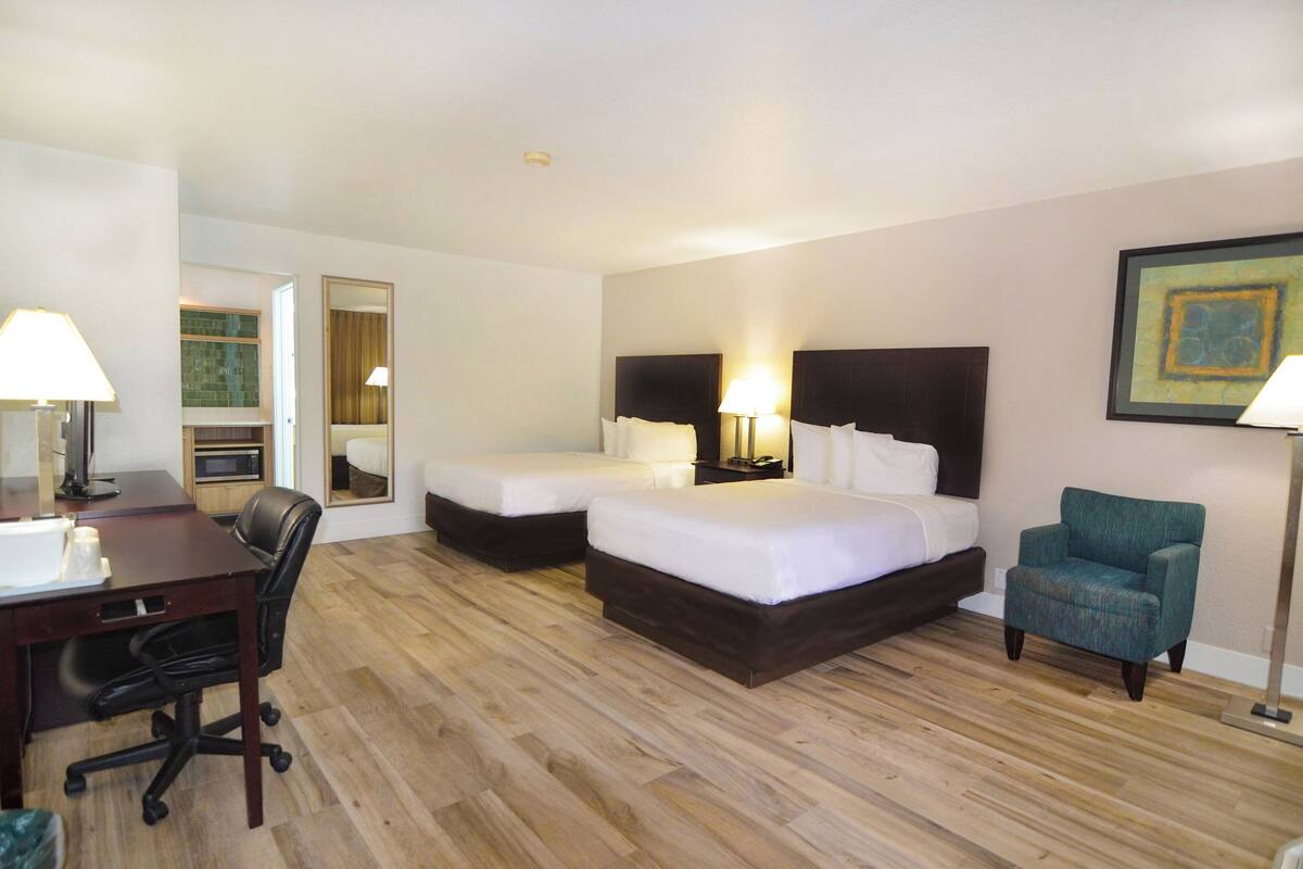 A hotel room with two beds, a desk, a chair, and a lamp.