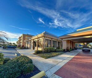 A modern hotel with a covered parking area, a well-maintained garden, and a clear blue sky.