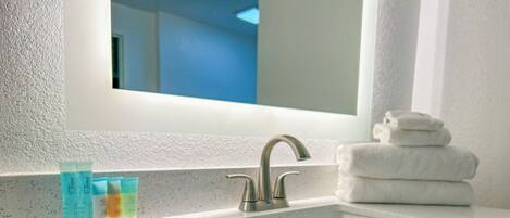 Un baño con encimera blanca con motas, un lavamanos moderno con un solo grifo y una pila de toallas blancas.